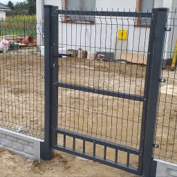 LEWSTAL PRZEMYSŁAW BABIŃSKI - Ciemnoszara brama panelowa z siatki, zamontowana na betonowej podmurówce, z widocznym mężczyzną w dżinsowej kurtce w tle, na placu budowy.