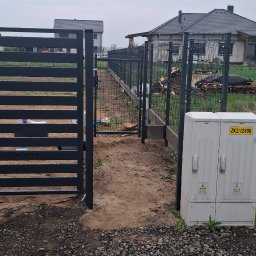 LEWSTAL PRZEMYSŁAW BABIŃSKI - Nowoczesne ogrodzenie panelowe w kolorze grafitowym, z elementami siatki. Widok na posesję z ulicy, w tle domy jednorodzinne. Słupki wbetonowane, teren wyrównany.