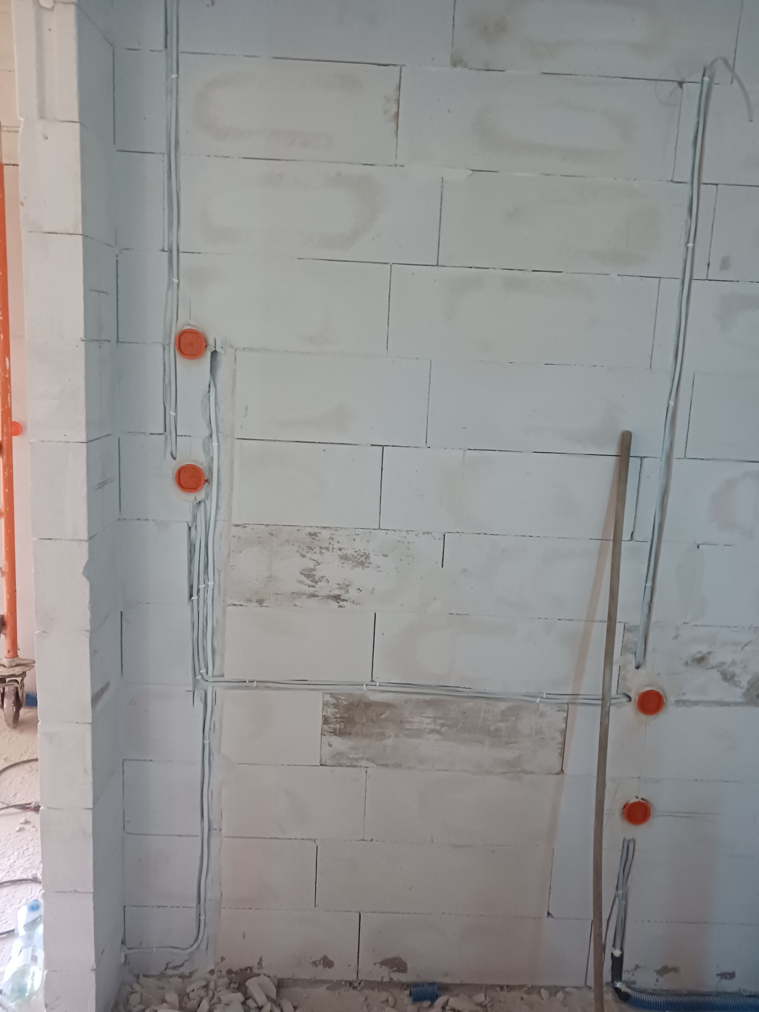 Świeżo położone przewody elektryczne w białej ścianie z betonu komórkowego z pomarańczowymi puszkami instalacyjnymi, widoczne niedoskonałości w ścianie, surowy stan wykończenia.