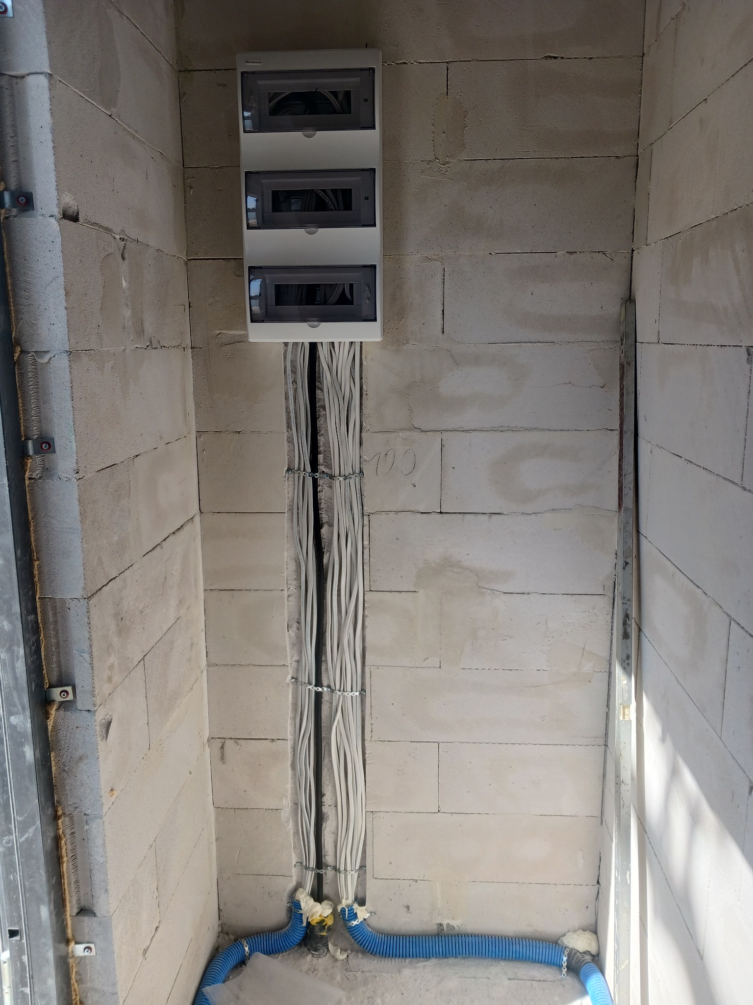 Rozdzielnica elektryczna z przewodami w ścianie z betonu komórkowego, zabezpieczone niebieskim peszlem, zamontowana w Lubszy.