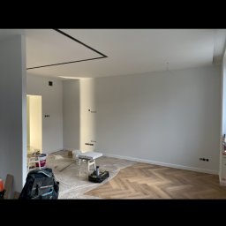 Nox Wykończenia Wnętrz Sp. z o.o. - Pokój w trakcie przygotowania do malowania, z podłogą zabezpieczoną folią, widoczne puszki z farbą, narzędzia i drabina.