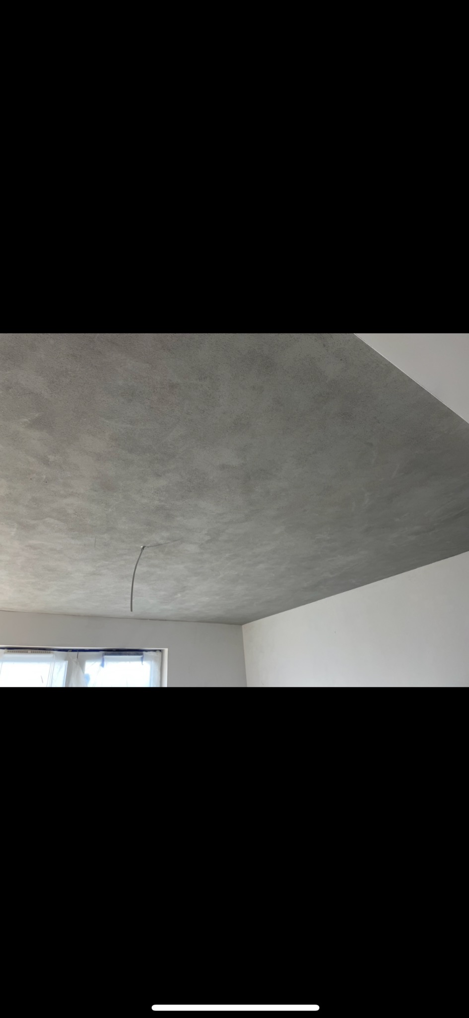 Szary sufit z widocznym przewodem elektrycznym, świeżo po nałożeniu gładzi, z oknem w tle zabezpieczonym folią.