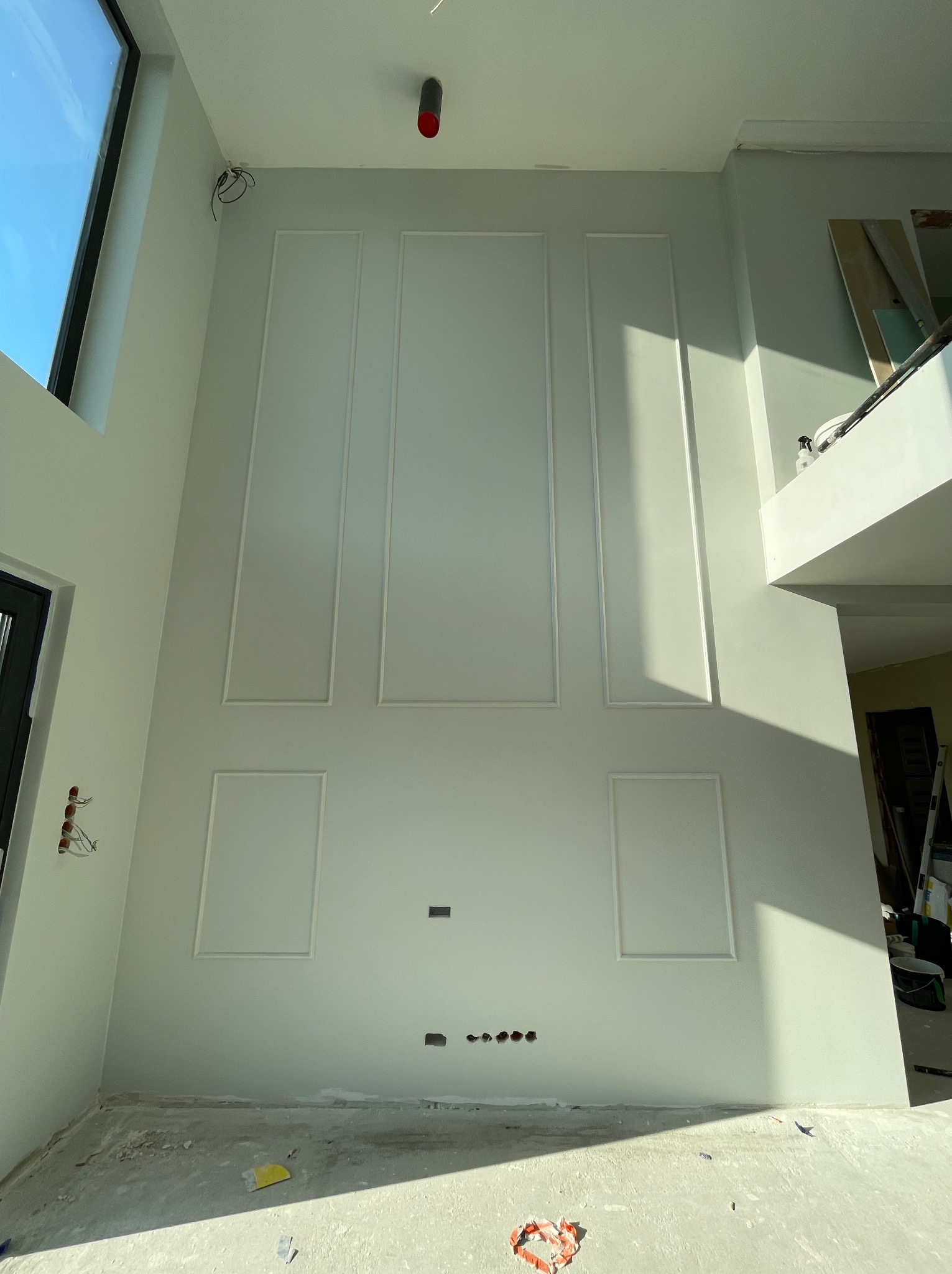 Wysoka ściana z dekoracyjnymi panelami i przygotowanymi otworami pod instalacje elektryczne w trakcie prac wykończeniowych w Krakowie.