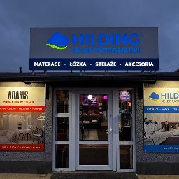 F.H.U. ADAMS MEBLE PIOTR ADAMSKI - Fasada sklepu meblowego Hilding i Adams Meble na Wymiar, prezentująca ekspozycje sypialni, salonu, kuchni i jadalni, z widocznymi reklamami materacy, łóżek, stelaży i akcesoriów.