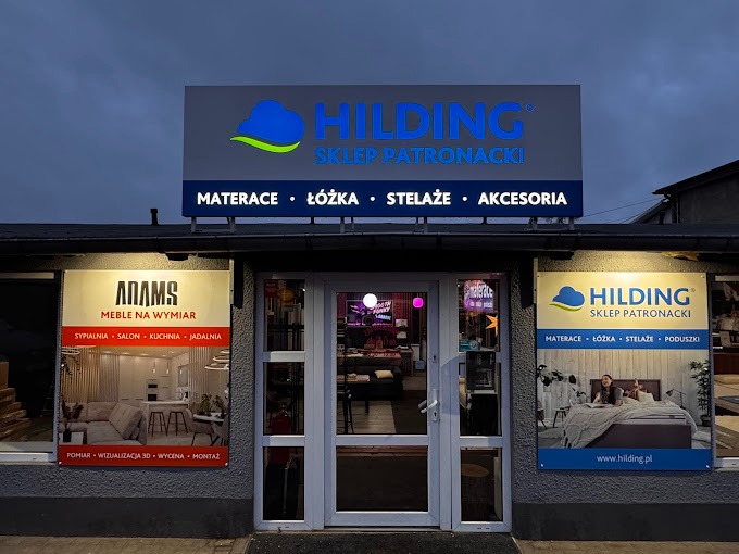 Fasada sklepu meblowego Hilding i Adams Meble na Wymiar, prezentująca ekspozycje sypialni, salonu, kuchni i jadalni, z widocznymi reklamami materacy, łóżek, stelaży i akcesoriów.