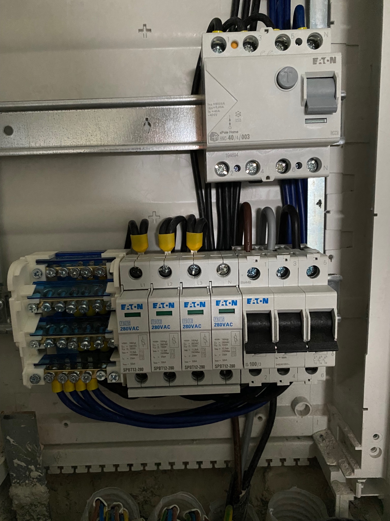 Szczegółowe ujęcie wnętrza skrzynki elektrycznej z zainstalowanymi bezpiecznikami EATON, przewodami z żółtymi końcówkami i wyłącznikiem różnicowoprądowym, widoczne oznaczenia L1, L2, L3, N.