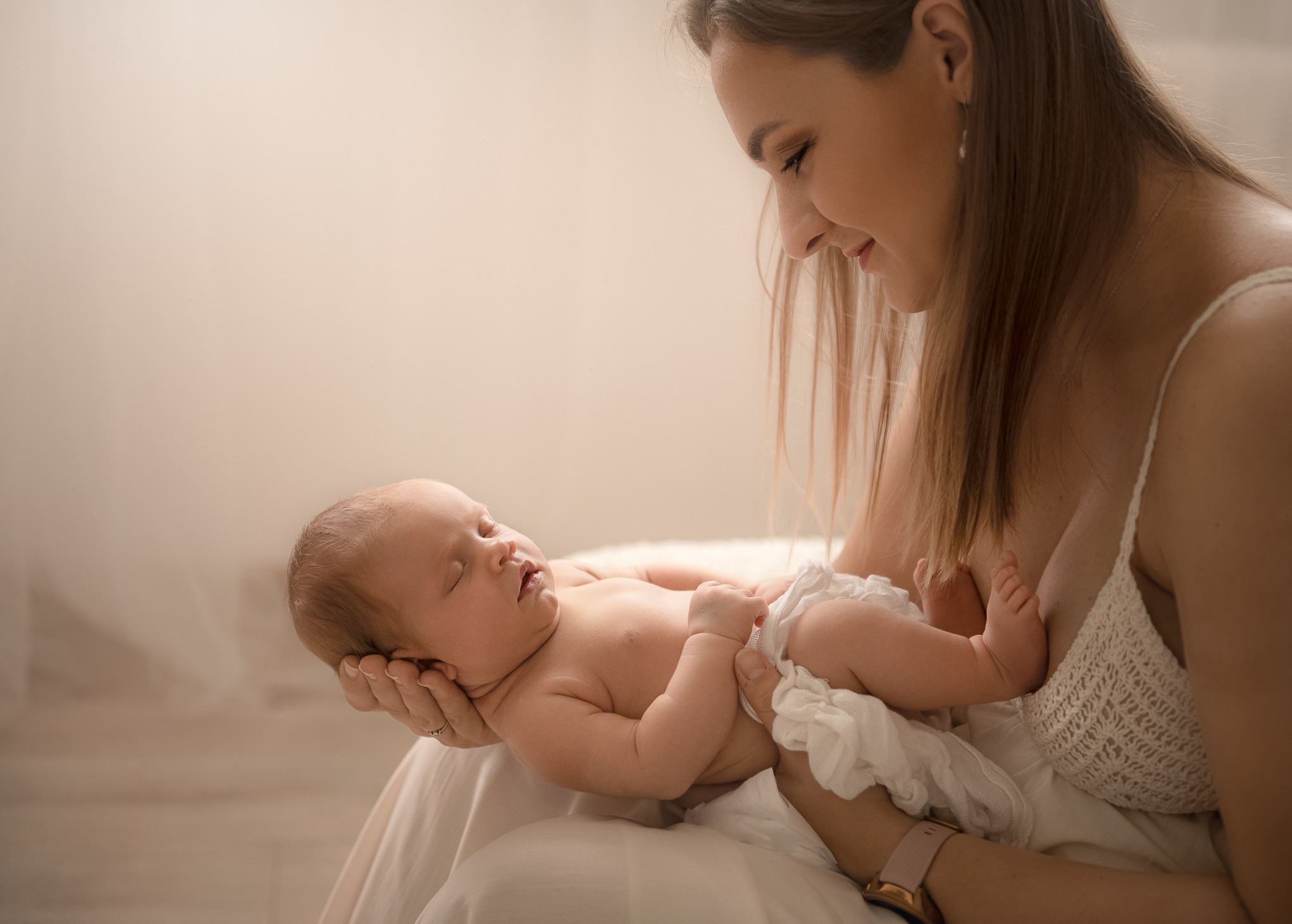 Delikatne ujęcie matki z noworodkiem w ramionach, spokojny sen dziecka w jasnym, naturalnym świetle.