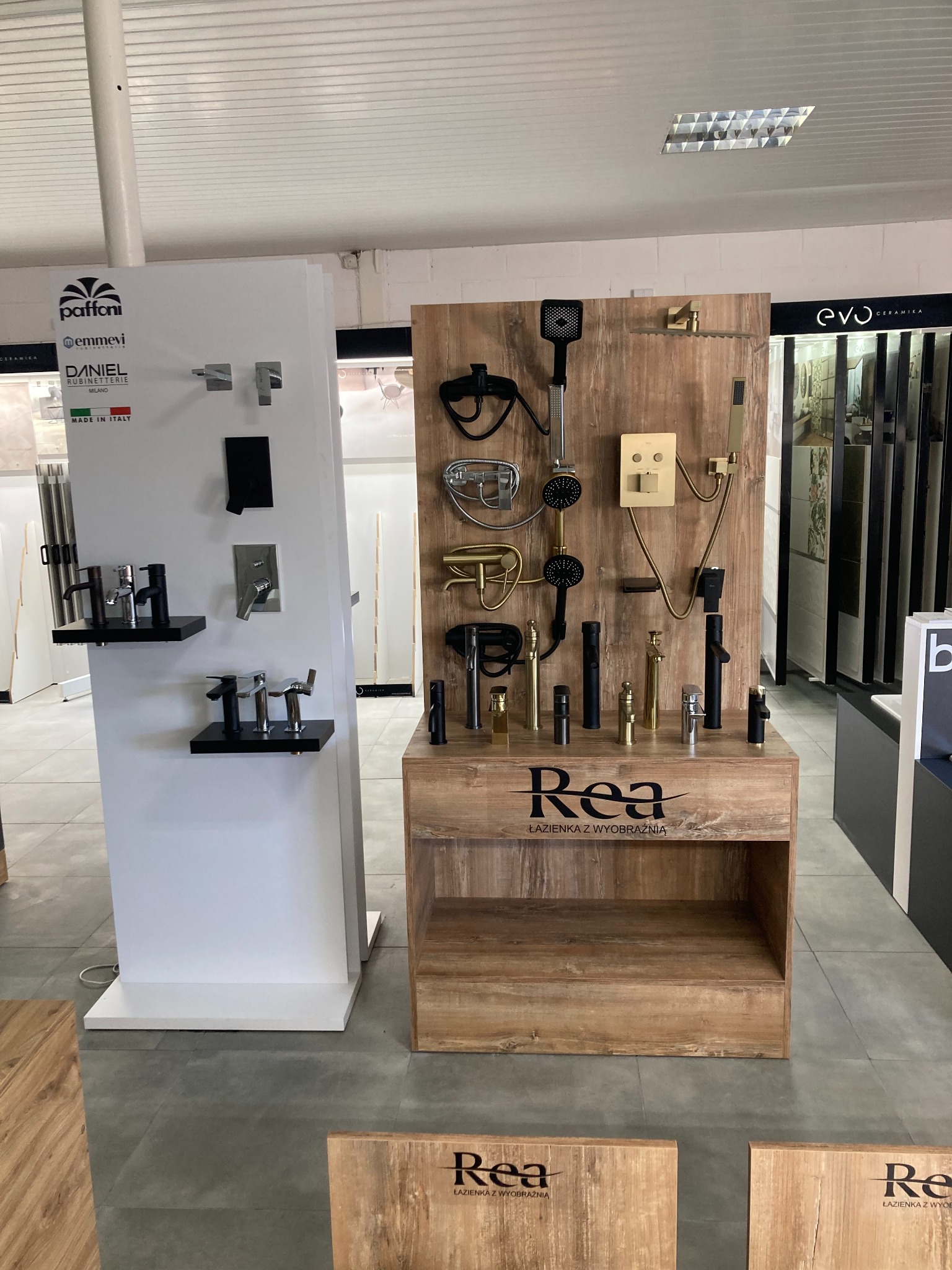 Ekspozycja baterii łazienkowych i prysznicowych różnych marek (Paffoni, Emmevi, Daniel, Rea, Evo Ceramika) prezentowana w salonie. Widoczne modele w kolorze czarnym, srebrnym i złotym...