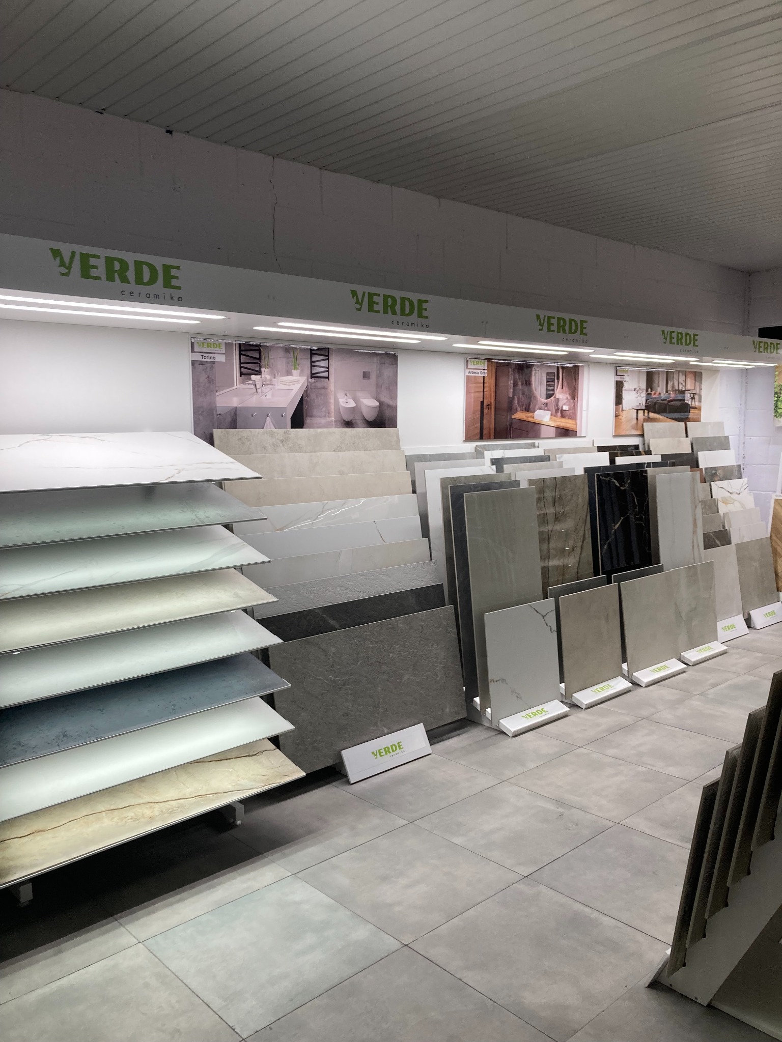 Ekspozycja płytek ceramicznych w sklepie Verde Ceramika, prezentacja różnych wzorów i kolorów na stojakach, w tle aranżacje łazienek i salonów.