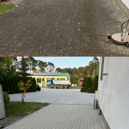 Mycie kostki brukowej - Zdjęcie 'przed i po' mycia kostki brukowej na posesji. Górna część kadru ukazuje zabrudzoną kostkę, dolna - czystą. W tle budynek i zieleń.
