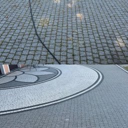 Mycie kostki brukowej - Częściowo wyczyszczona kostka brukowa z widocznym wężem do mycia. Na dole kostka po czyszczeniu, na górze przed. Widok z góry na szarą kostkę.