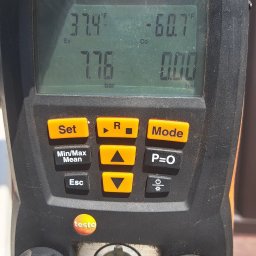 DARIUSZ KRÓL - Cyfrowy manometr Testo 550, wskazujący wartości ciśnienia i temperatury, z widocznymi przyłączami i przyciskami funkcyjnymi, uchwycony w trakcie pomiaru, z fragmentem roboczej rękawicy w tle.