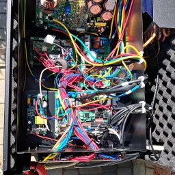 DARIUSZ KRÓL - Wnętrze obudowy urządzenia z widocznymi płytkami drukowanymi, kondensatorami i wiązkami kolorowych przewodów, z multimetrem leżącym obok na brukowanej powierzchni.