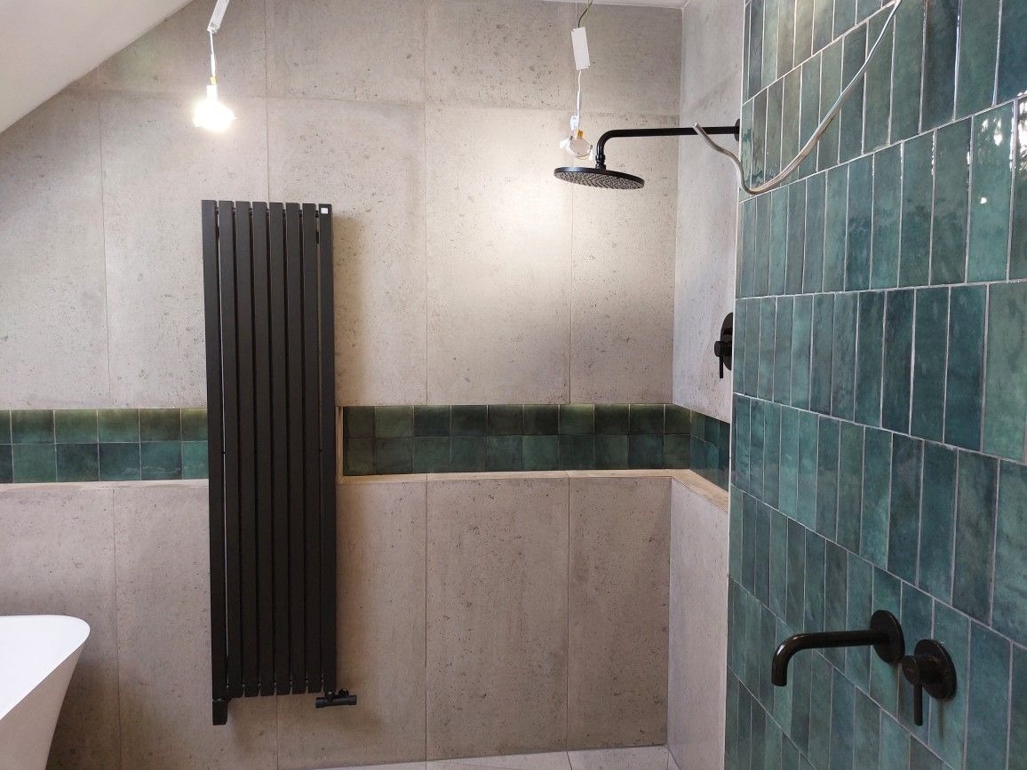 Nowoczesna łazienka z zielonymi, pionowo ułożonymi płytkami, czarną armaturą i grzejnikiem drabinkowym, widoczna biała wanna.