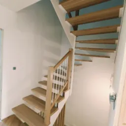 Jasne drewniane schody z białymi balustradami w nowoczesnym wnętrzu, widok z góry na dół, parkiet ułożony w jodełkę.