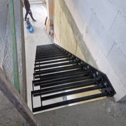 LOFT WELDING Krystian Kudela - Surowe schody z czarnego metalu w trakcie montażu w surowym wnętrzu budynku, widok z góry na konstrukcję z widocznymi śrubami mocującymi, na tle betonowych ścian i podłogi, z narzędziami w tle.