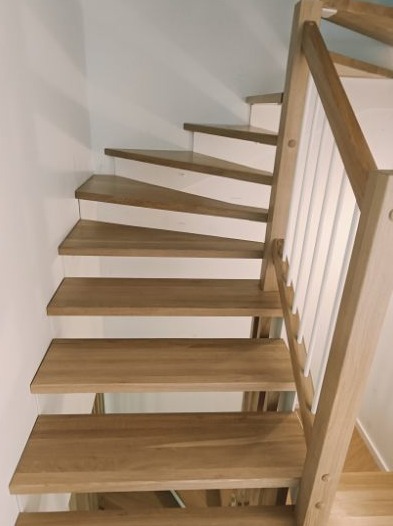 Kątowe ujęcie drewnianych schodów z białymi podstopnicami i drewnianą balustradą z białymi pionowymi elementami, widoczne z dołu.