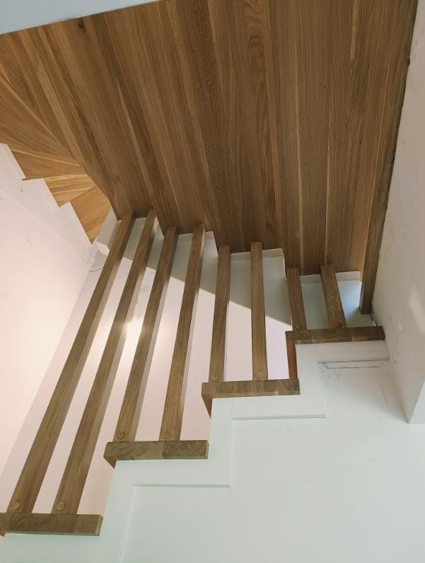 Nowoczesne schody z białymi stopniami i drewnianą balustradą z pionowych belek, widok z dołu, drewniany sufit pod schodami.