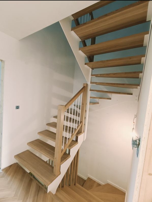 Jasne drewniane schody z białymi balustradami w nowoczesnym wnętrzu, widok z góry na dół, parkiet ułożony w jodełkę.