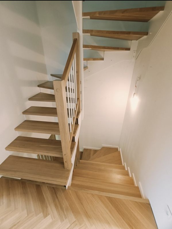 Drewniane schody z białymi balustradami i parkietem ułożonym w jodełkę, widok z góry.