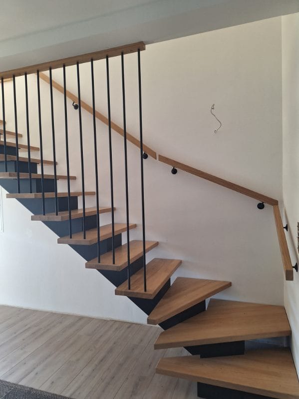 Nowoczesne schody z drewnianymi stopniami i czarną metalową konstrukcją oraz drewnianą poręczą, zamocowaną do ściany. Minimalistyczny design.
