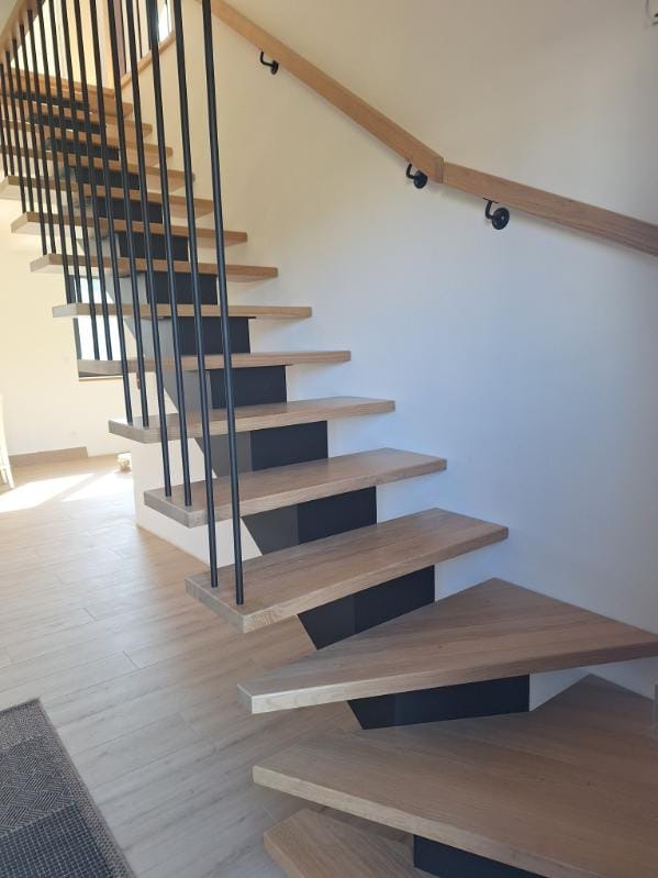 Nowoczesne schody z drewnianymi stopniami i czarnymi metalowymi wspornikami. Minimalistyczna balustrada z drewnianą poręczą i czarnymi, pionowymi prętami.
