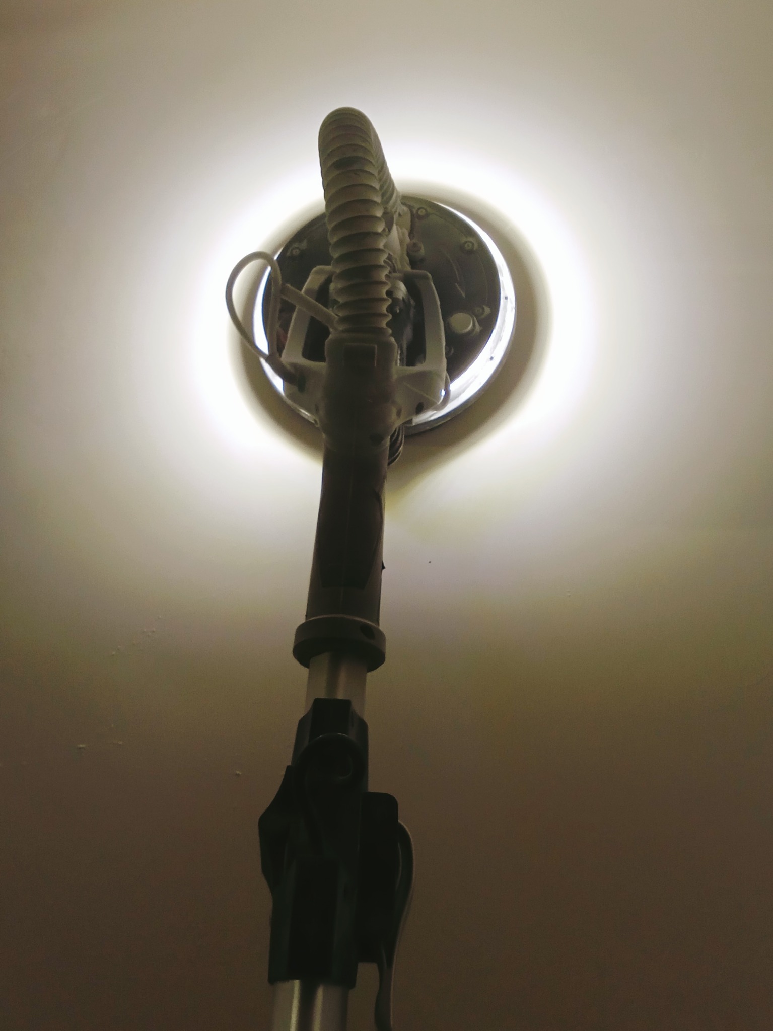 Szlifierka do gładzi gipsowych oświetlająca sufit podczas pracy, widok z dołu.