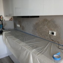 HIEX - Kuchnia w trakcie prac wykończeniowych: zabezpieczony blat folią, ściana z dekoracyjnym tynkiem strukturalnym z ornamentem, gniazdko elektryczne.