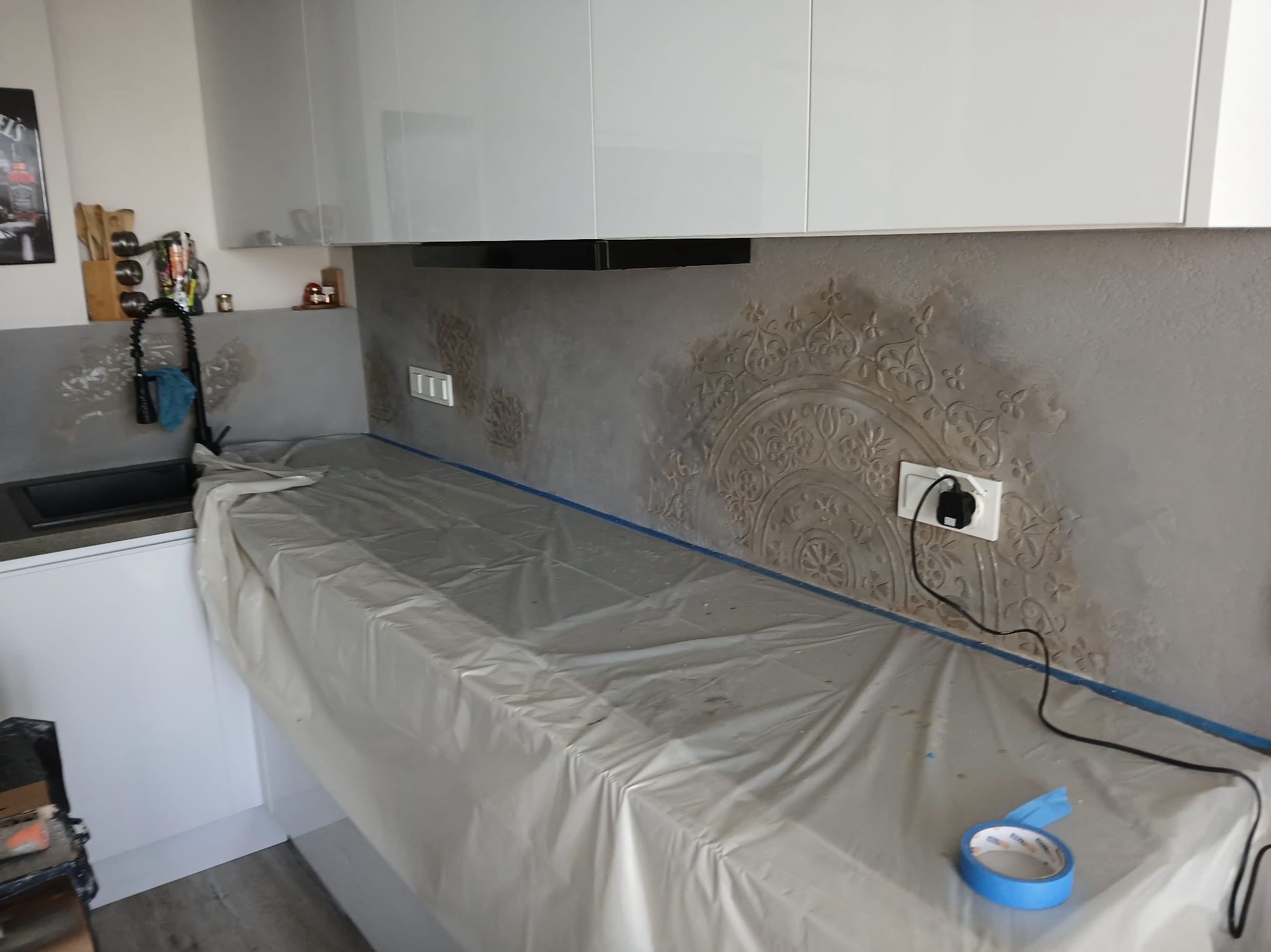 Kuchnia w trakcie prac wykończeniowych: zabezpieczony blat folią, ściana z dekoracyjnym tynkiem strukturalnym z ornamentem, gniazdko elektryczne.