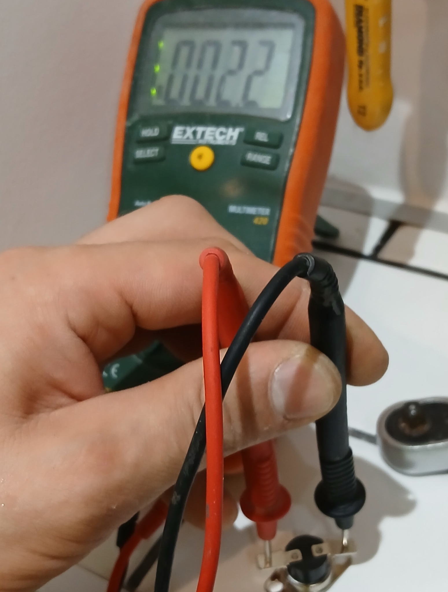 Pomiar multimetrem wartości na termistorze. Widoczny wyświetlacz, przewody pomiarowe w dłoni montera i element elektroniczny. Precyzyjny pomiar parametrów.