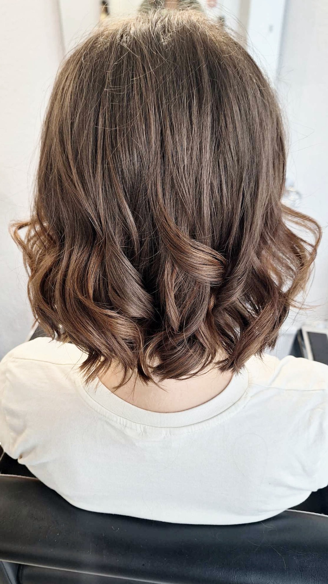 Krótkie, brązowe włosy z delikatnymi falami, widok z tyłu, świeżo po stylizacji.