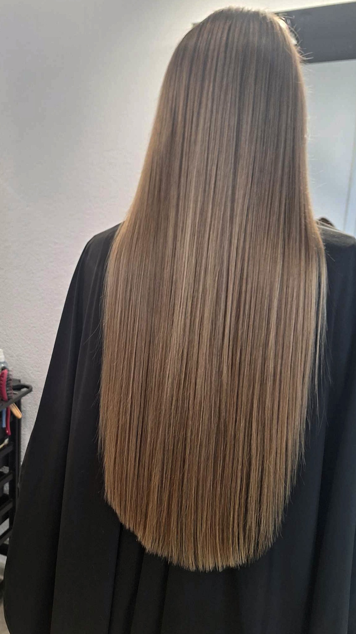 Długie, proste, brązowe włosy z delikatnymi refleksami, widoczne od tyłu, okryte czarną peleryną ochronną.