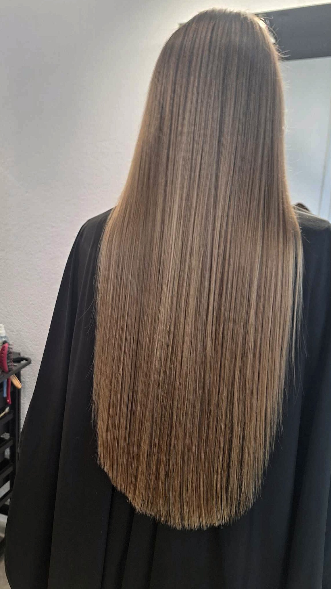 Długie, proste, brązowe włosy z subtelnymi refleksami, widziane od tyłu, okryte czarną peleryną ochronną.