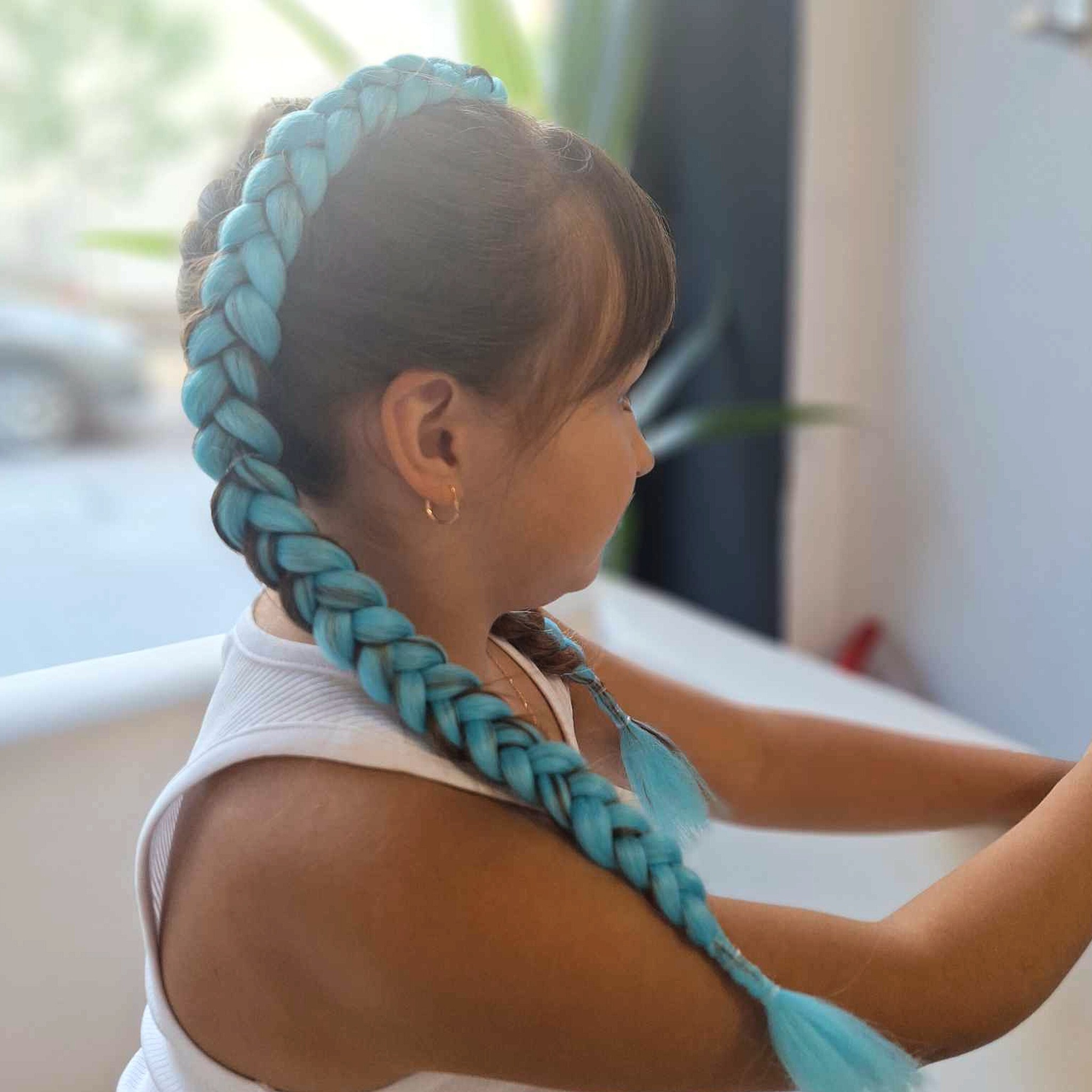 Dziewczynka z zaplecionym warkoczem z niebieskich włosów syntetycznych, widok z profilu, złote kolczyki koła.