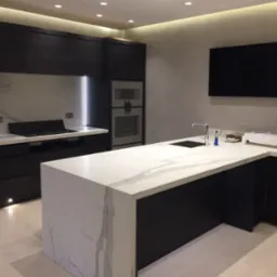 Nowoczesna kuchnia z czarnymi szafkami i blatem z białego kamienia z wyraźnym marmurkowym wzorem, oświetlenie LED podkreśla przestrzeń nad płytą grzewczą.