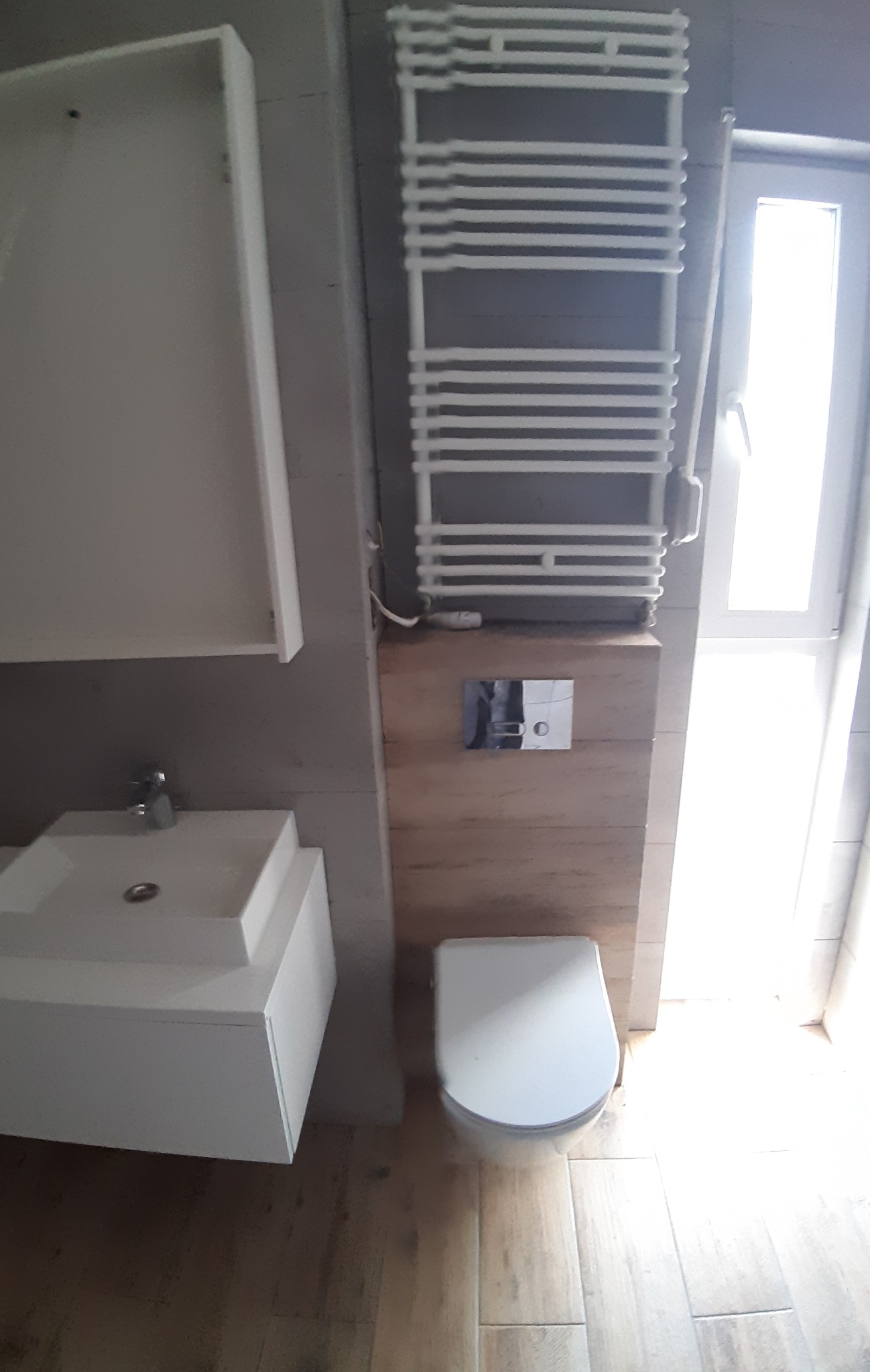 Nowoczesna łazienka z umywalką nablatową, grzejnikiem drabinkowym i podwieszaną toaletą. Drewnopodobna zabudowa pod toaletą.