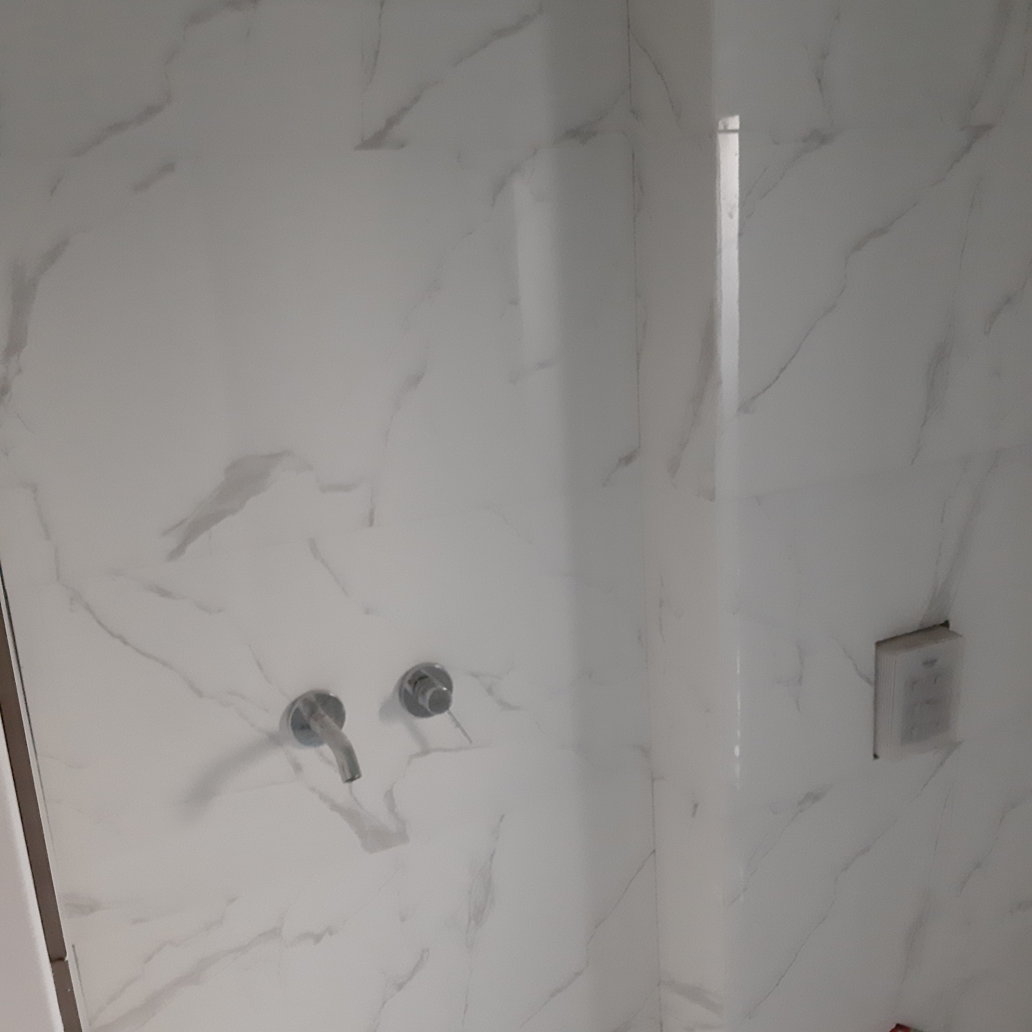 Biała ściana w łazience z marmurowym wzorem, widoczne dwa krany i gniazdko elektryczne