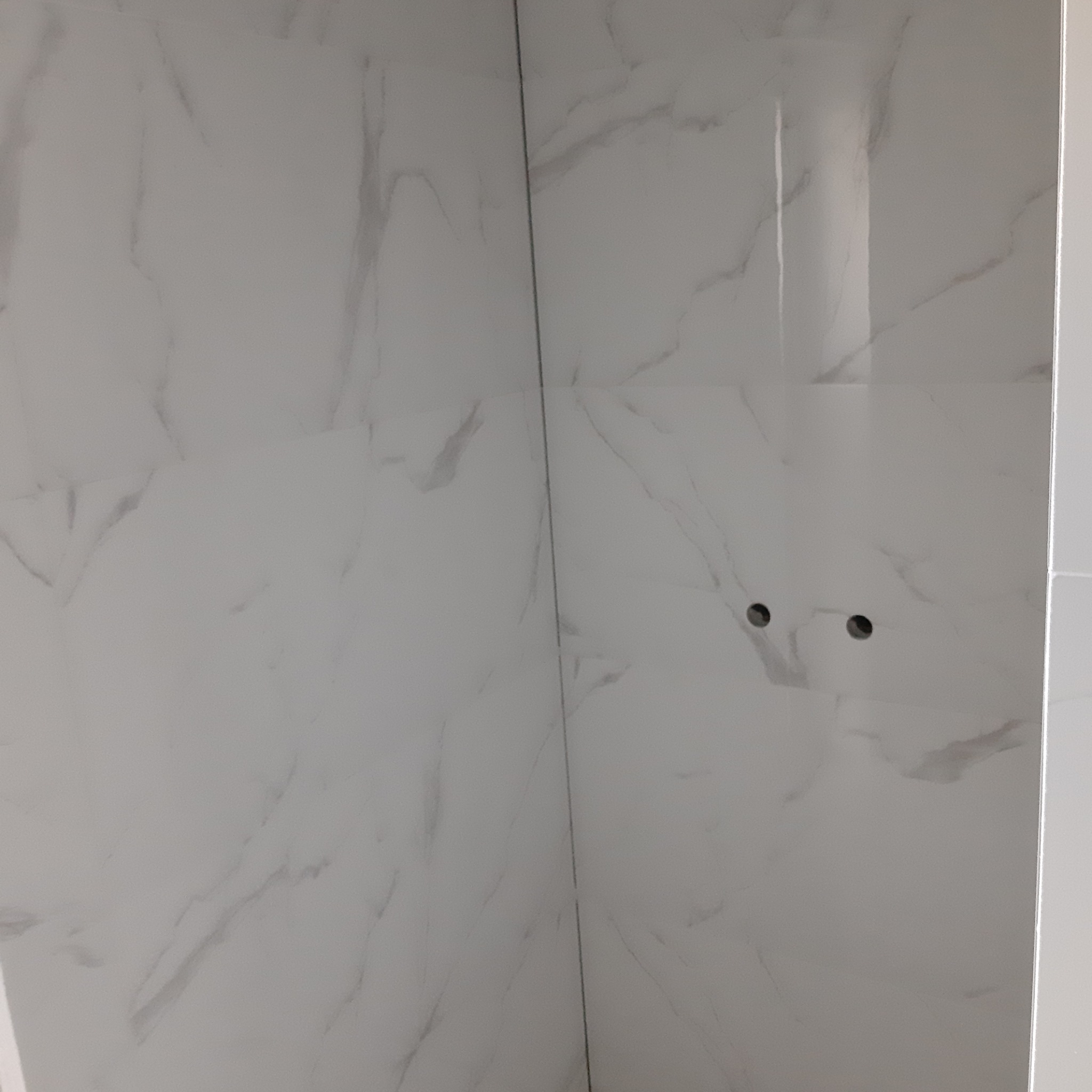 Ściana wyłożona białymi płytkami imitującymi marmur, z wywierconymi dwoma otworami pod instalację.