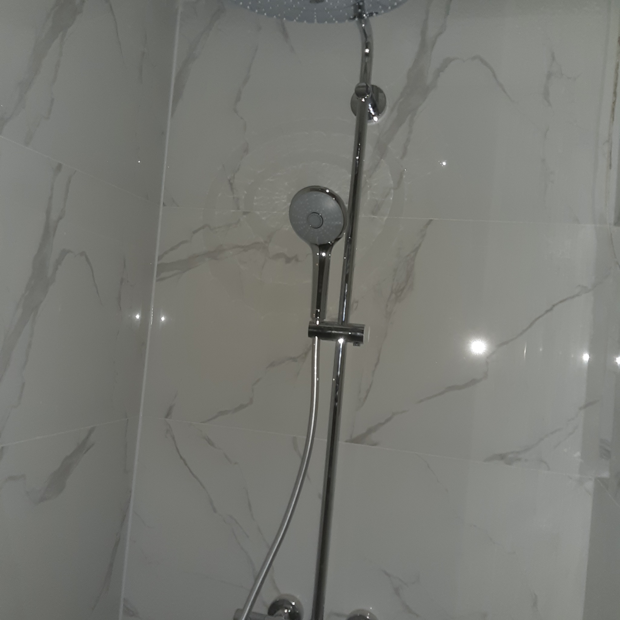 Nowoczesna kabina prysznicowa z chromowaną armaturą i białymi płytkami imitującymi marmur.