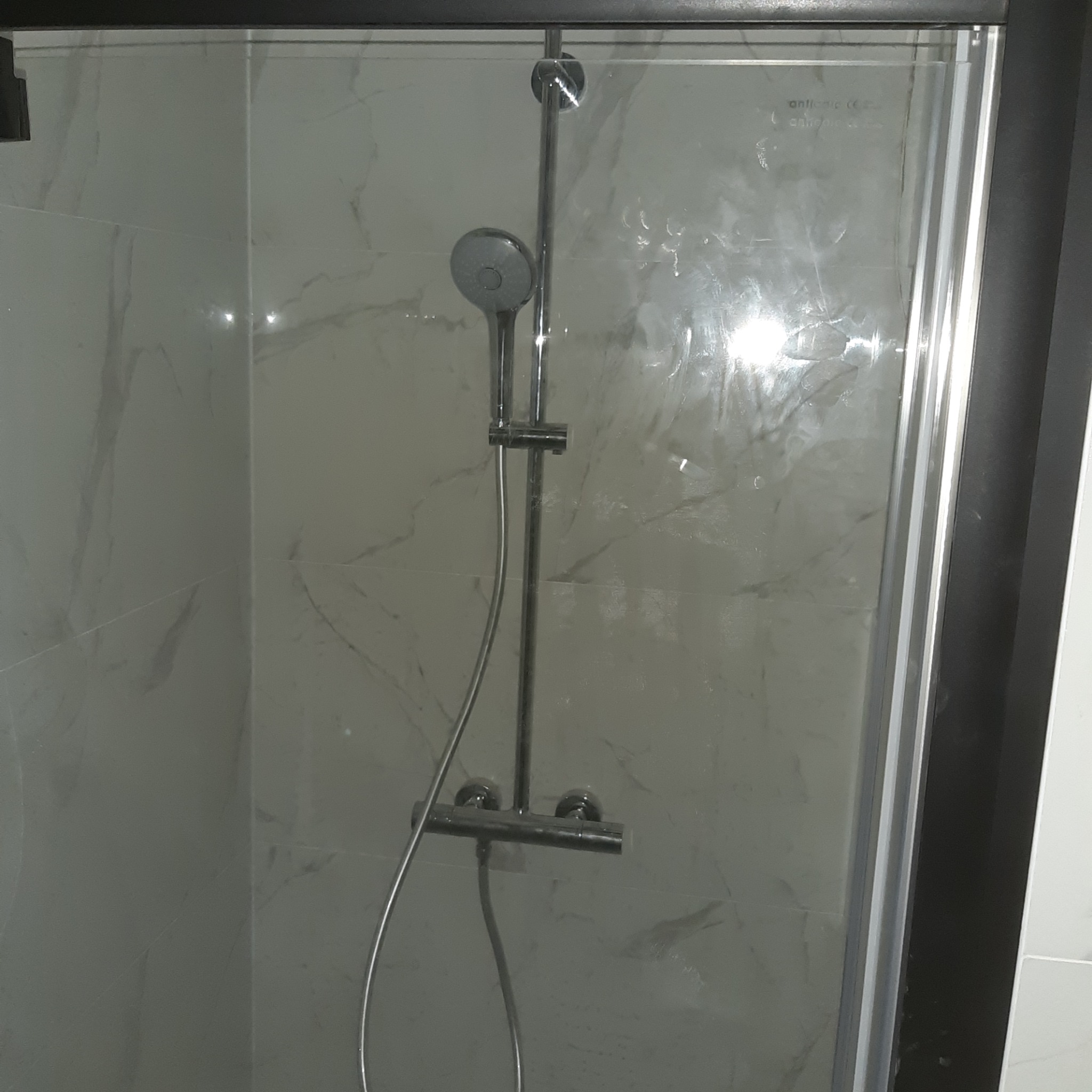 Nowoczesna kabina prysznicowa z chromowaną armaturą na tle marmurowych płytek ściennych, widok przez lekko zaparowaną szybę.