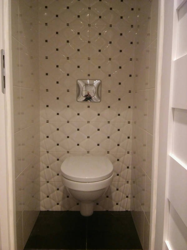 Kompaktowa toaleta podwieszana w Poznaniu, z czarną podłogą i białymi płytkami ściennymi z dekoracyjnym wzorem w romby z czarnymi akcentami, zamontowana między białymi drzwiami i ścianą.