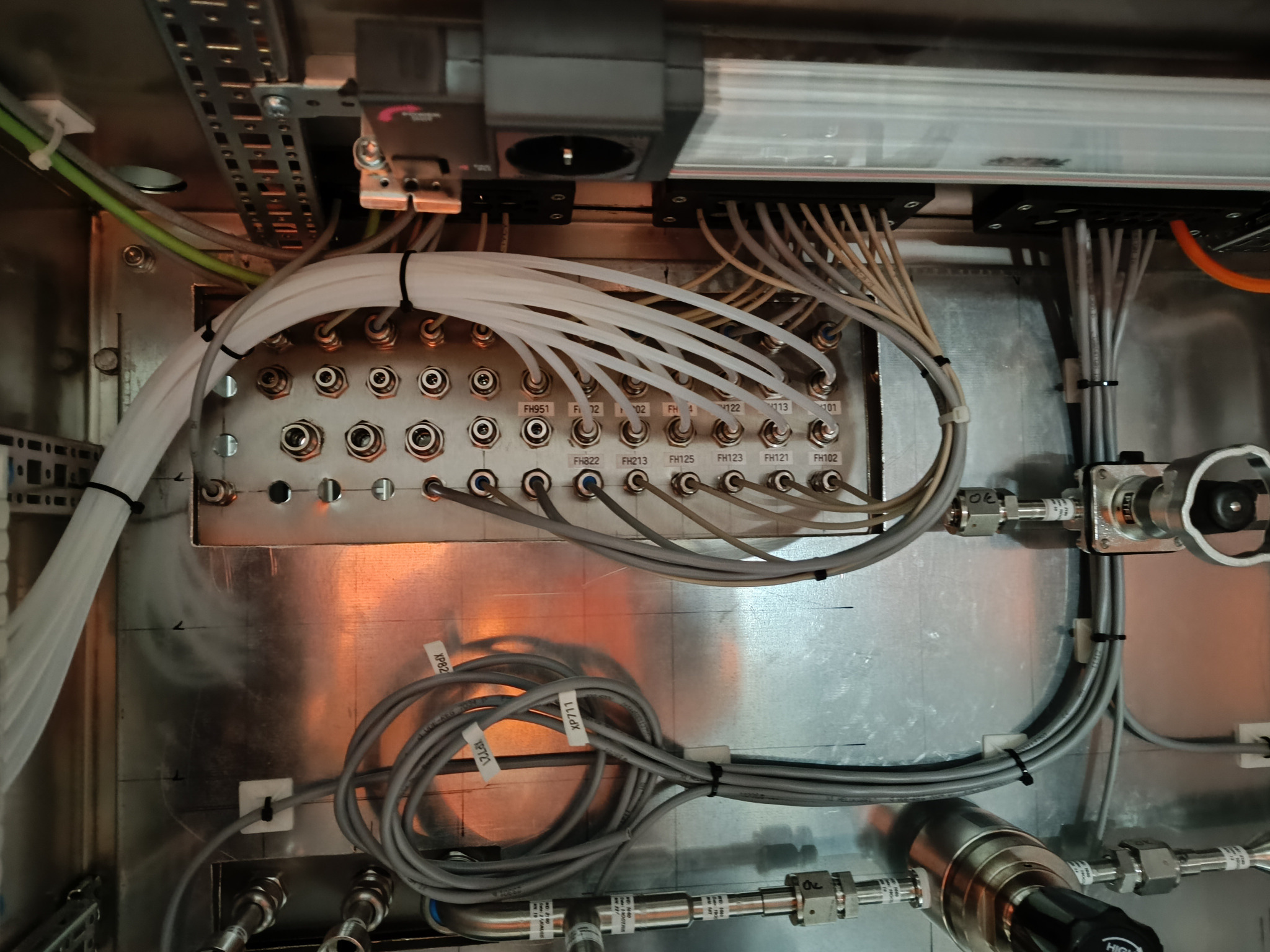 Wnętrze szafy sterowniczej z licznymi przewodami i złączami, widoczne etykiety identyfikacyjne przewodów i portów, metalowa konstrukcja z elementami montażowymi.