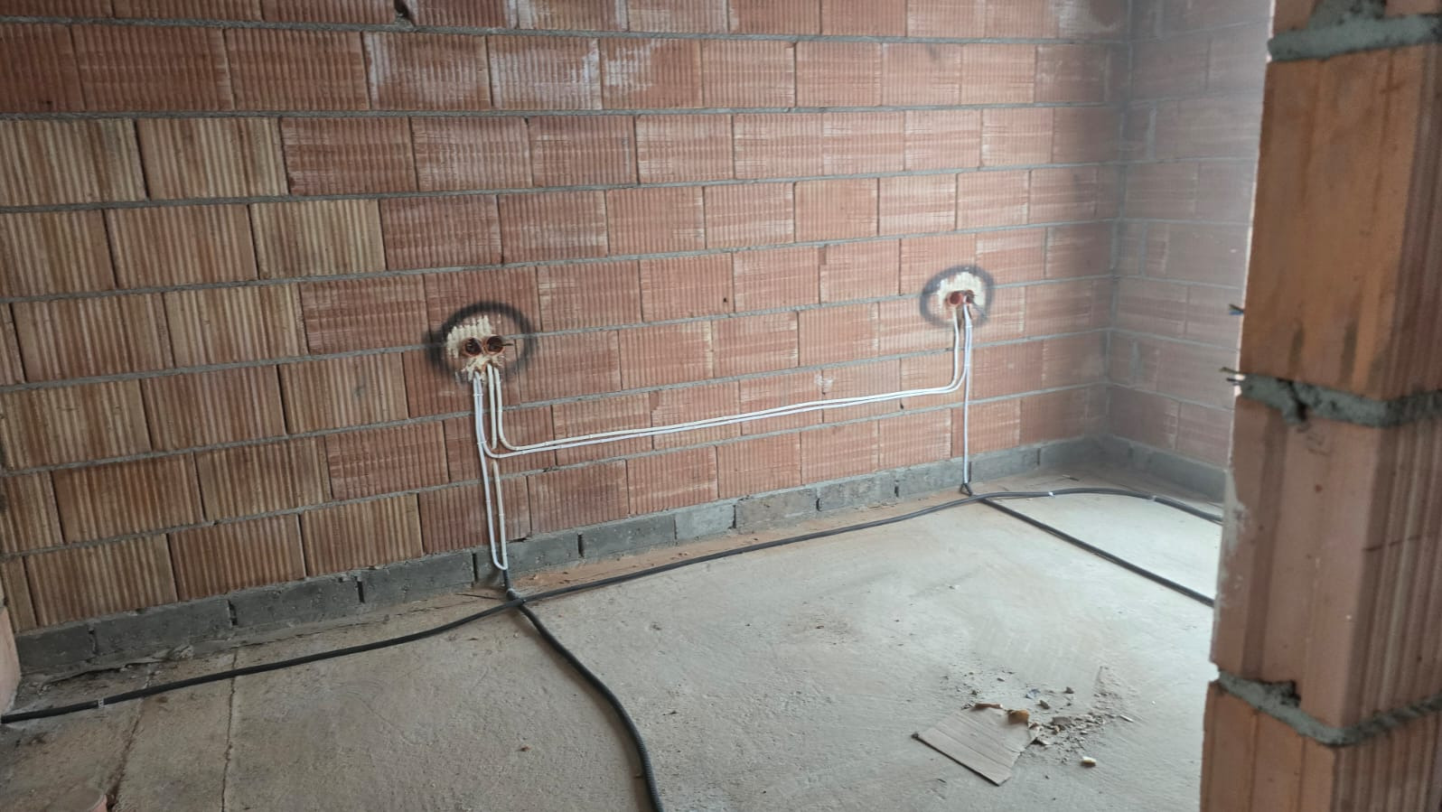 Instalacja elektryczna w surowym wnętrzu: przewody w ścianie z cegły dziurawki, przygotowane gniazdka, kable na podłodze. Widok na wczesny etap prac.