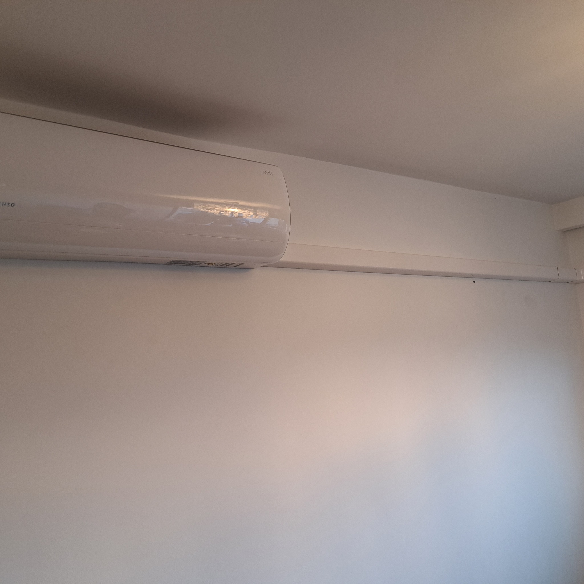 Biały klimatyzator Vesta zamontowany na białej ścianie z widoczną listwą maskującą przewody.