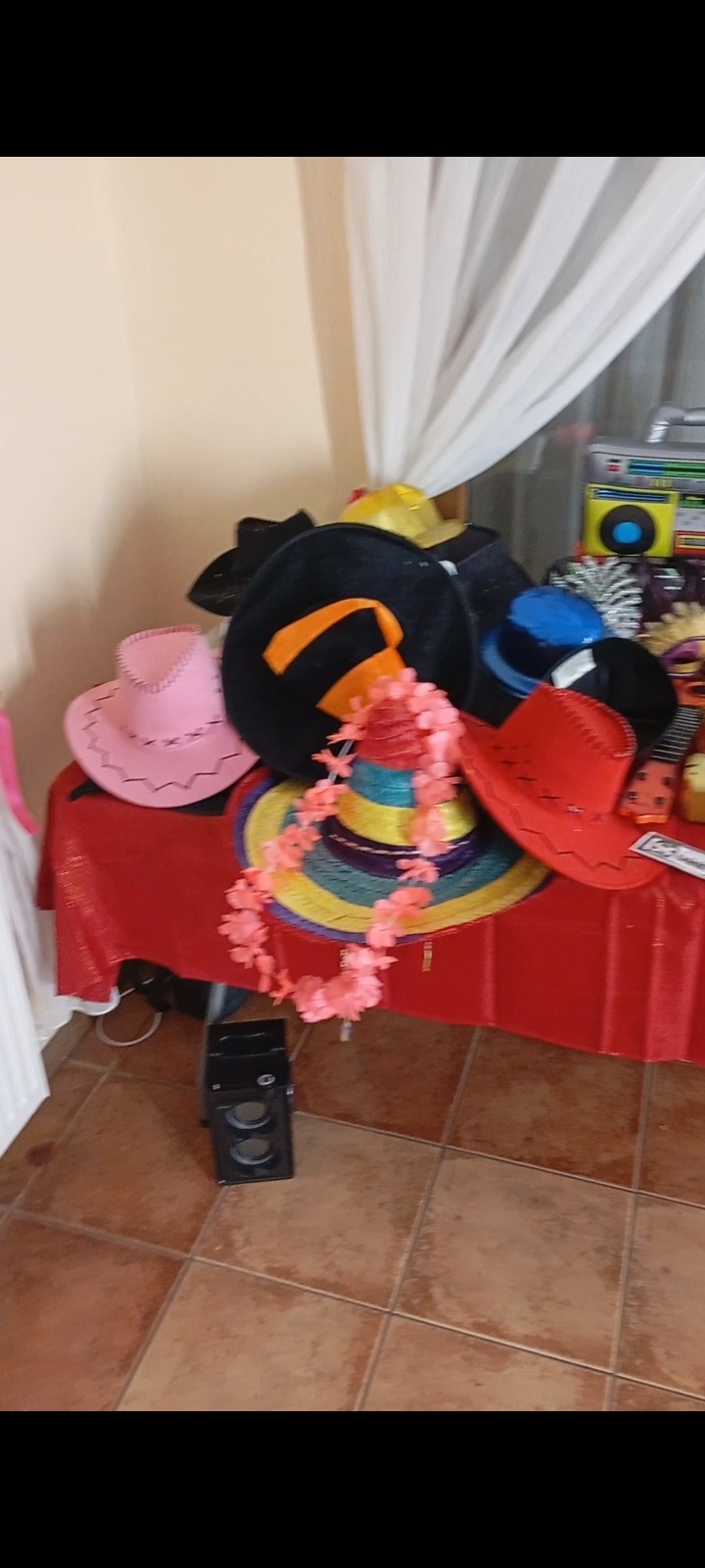 Różnokolorowe kapelusze i hawajski naszyjnik na czerwonym stole, przygotowane jako rekwizyty do sesji zdjęciowej.