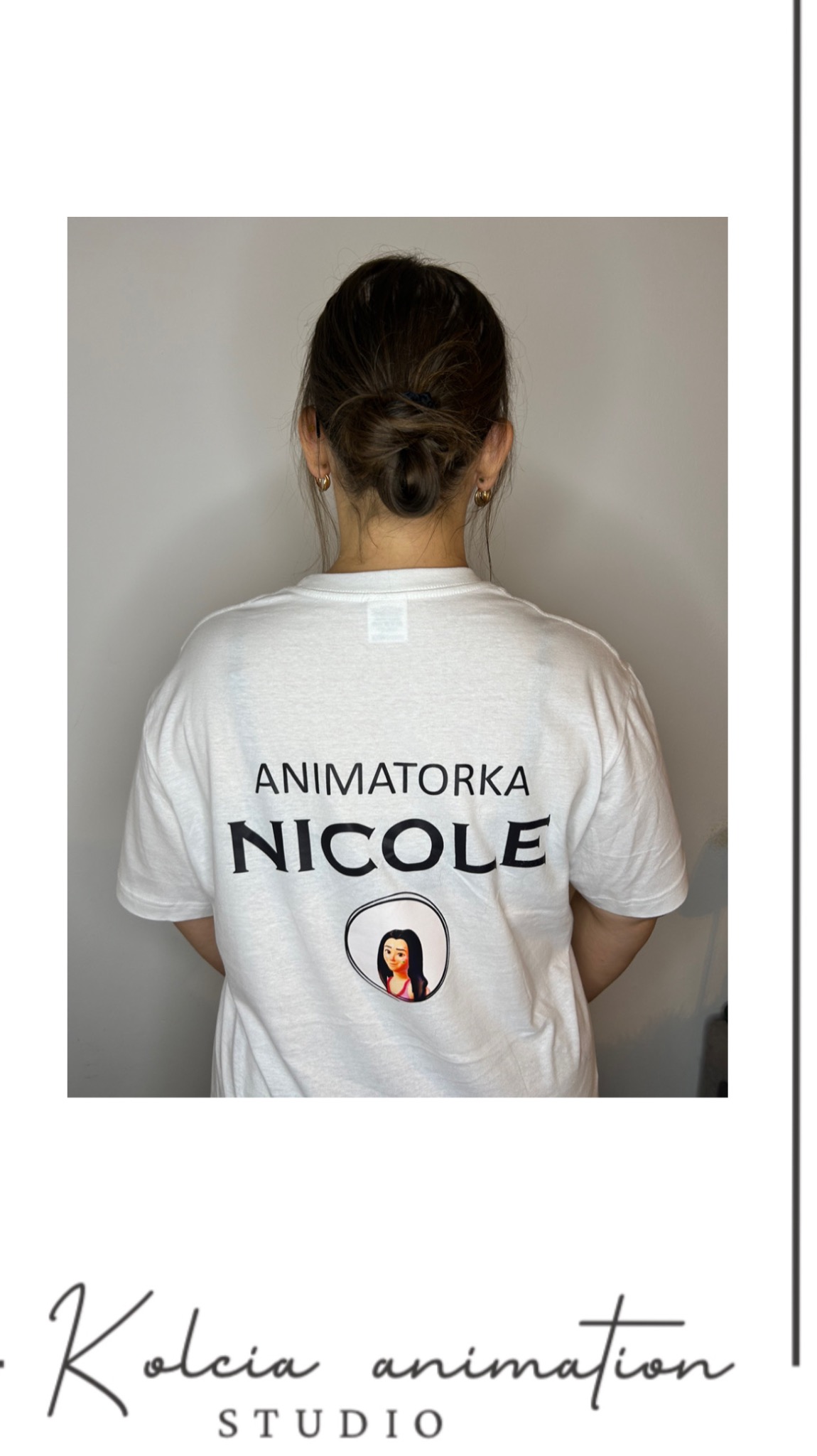 Kobieta, widziana od tyłu, w białej koszulce z napisem 'Animatorka Nicole' i okrągłym nadrukiem z wizerunkiem kobiety, włosy upięte w kok.