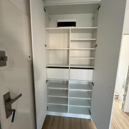 FIX WOOD ZABUDOWY MEBLOWE - Wnętrze białej szafy wnękowej z otwartymi drzwiami, widoczne półki i dwie szuflady, zamek w drzwiach wejściowych po lewej stronie.