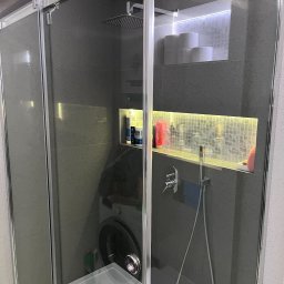 TANIE SPRZĄTANIE Wiktoria Krośnicka - Szklana kabina prysznicowa z deszczownicą i wnękami w ścianie wyłożonymi mozaiką, podświetlonymi ledami, z widoczną pralką w tle.