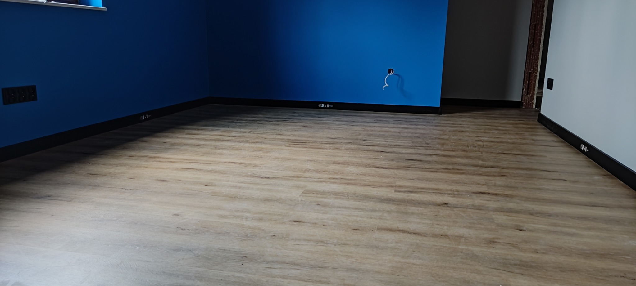 Ułożone panele podłogowe w pokoju z niebieską ścianą i widocznymi puszkami elektrycznymi.