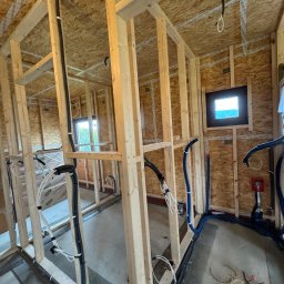 Instalatorstwo Elektryczne Kacper Szymala - Wnętrze w trakcie budowy z widocznymi drewnianymi konstrukcjami ścian i stropu. Ułożone przewody elektryczne i instalacyjne w peszlach. Małe okno w ścianie.